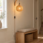 Bamboe wandlamp in een lichte hal boven een houten bankje, overdag