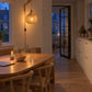 Bamboe wandlamp boven een eikenhouten eettafel met bankje in een lichte keuken, 's avonds