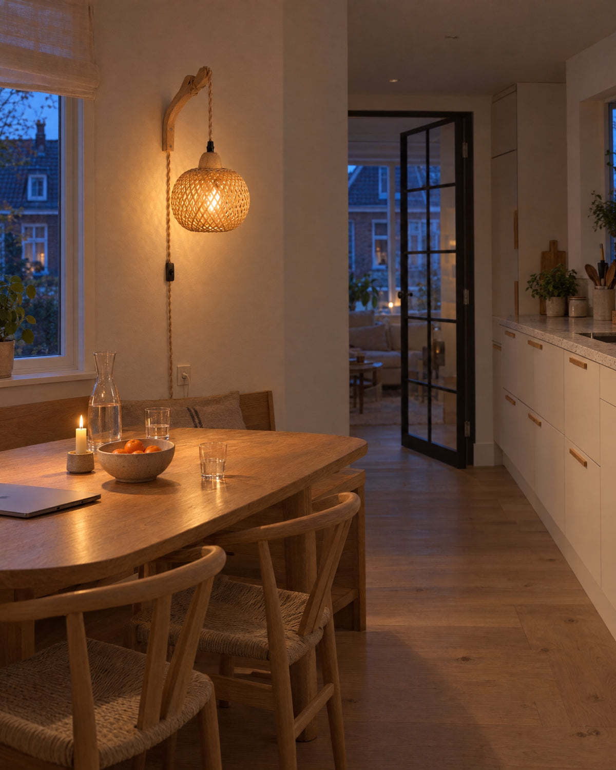 Bamboe wandlamp boven een eikenhouten eettafel met bankje in een lichte keuken, 's avonds